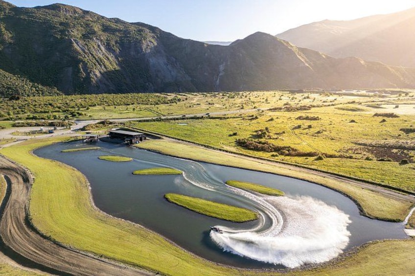 A river with a boat creating a wake, surrounded by green fields and mountains. 3