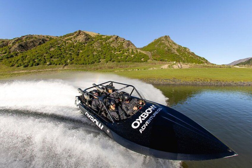 A speedboat with 'OXBOM' and 'ADVENTURE' on its side, moving swiftly on water with a mountainous landscape in the background. 4