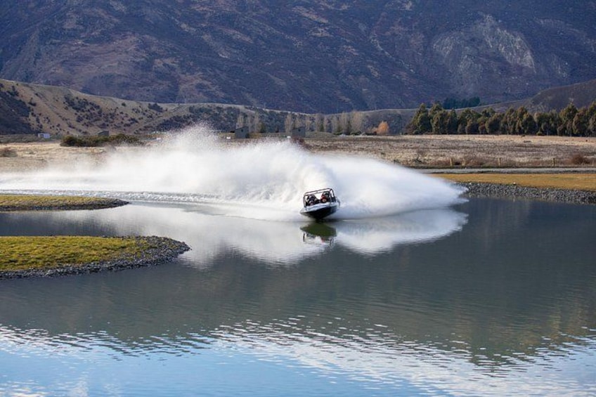 A boat creating a large splash on a calm lake with mountains in the background. 5
