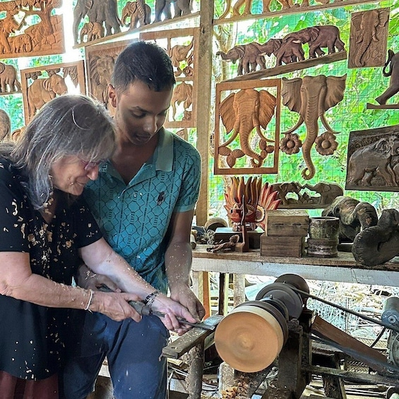 Two people working on a lathe with wooden elephant carvings in the background. 4