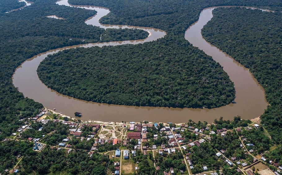 Eine Vogelperspektive auf einen Fluss, der sich durch ein dicht bewaldetes Gebiet schlängelt, mit einer kleinen Siedlung an seinem Unterlauf. 5