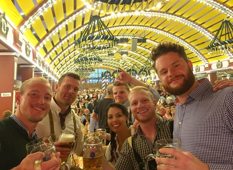 Ryhmä ihmisiä Oktoberfest-juhlissa, heidän ympärillään perinteisiä baijerilaisia telttakatoksia ja koristeita. 3