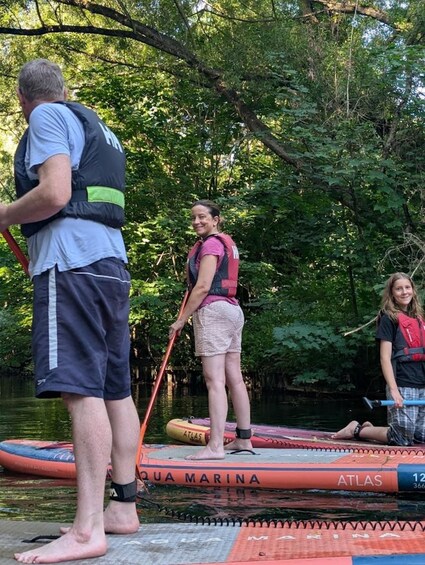 Three people on a paddleboard in a forested area with a river. 2
