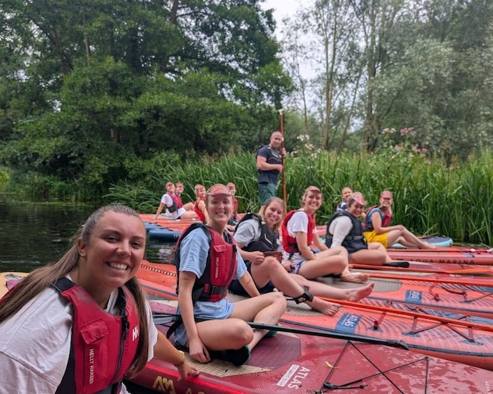 A group of people sitting on red kayaks on a calm river surrounded by lush greenery. 1