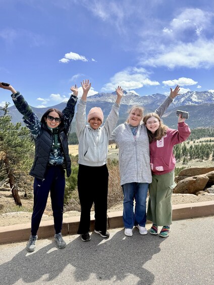 Four people standing on a roadside with a mountainous landscape in the background. 5