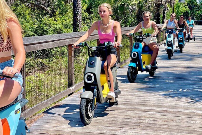 Menschen fahren mit Elektrorollern auf einer Holzpromenade. 5