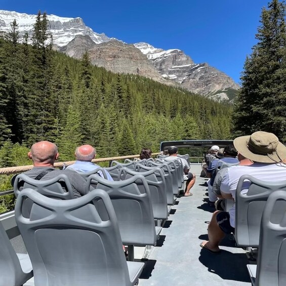 A group of people seated on a tour bus with a mountainous landscape in the background. 3