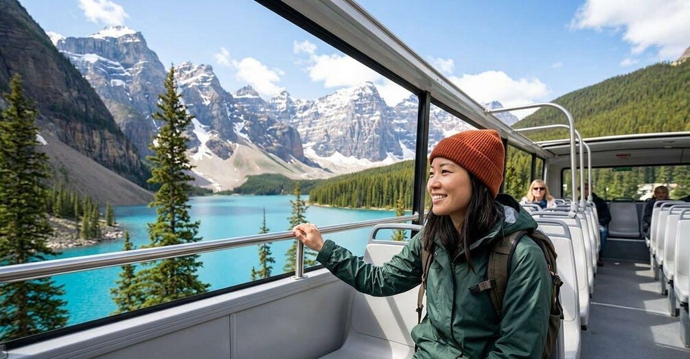 A person in a green jacket and red beanie looking out of a bus window at a mountain lake with snow-capped peaks. 2