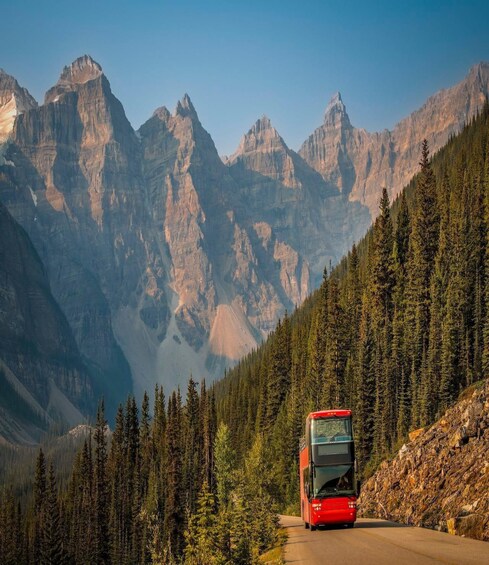 A red bus on a mountain road with dense forests and rugged peaks in the background. 4