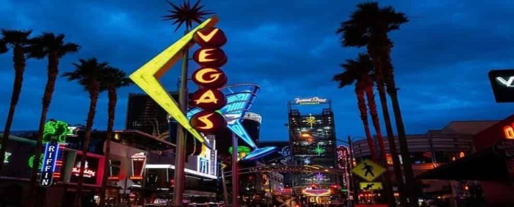 A neon sign reading "VEGAS" with palm trees and illuminated buildings in the background. 1