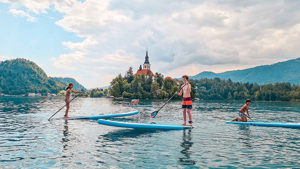 People paddleboarding on a lake with a church on a hill in the background. 5