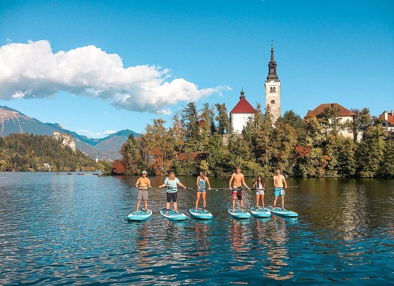 People paddleboarding on a lake with a church and mountains in the background. 2