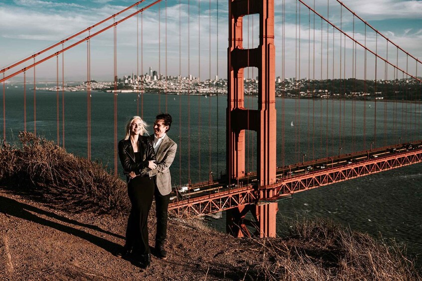Pariskunta seisoo kukkulalla, jolta avautuu näkymä Golden Gate -sillalle, ja kaupungin siluetti näkyy taustalla. 1