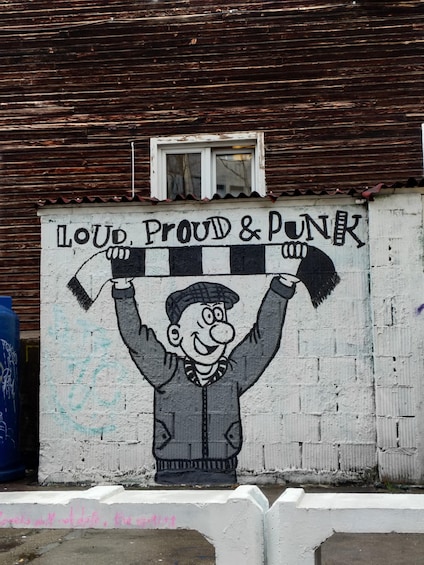 A wall with a mural of a man holding a checkered scarf and a sign that reads 'LOUD, PROUD & PUNK.' 5