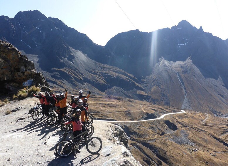 A group of cyclists on a mountain trail with rocky terrain and a winding road. 1