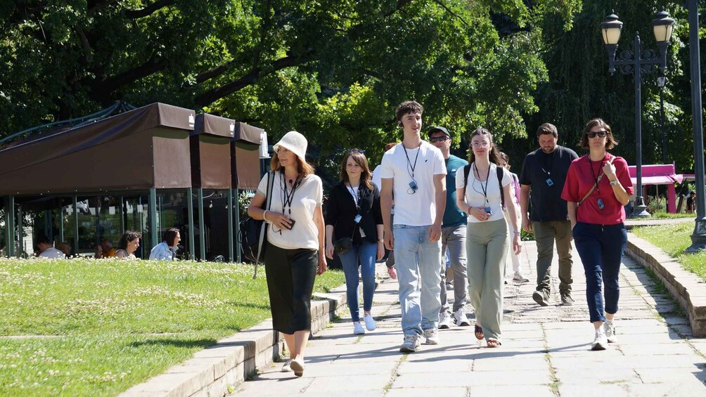 A group of people walking on a paved path in a park with trees and a covered area in the background. 5