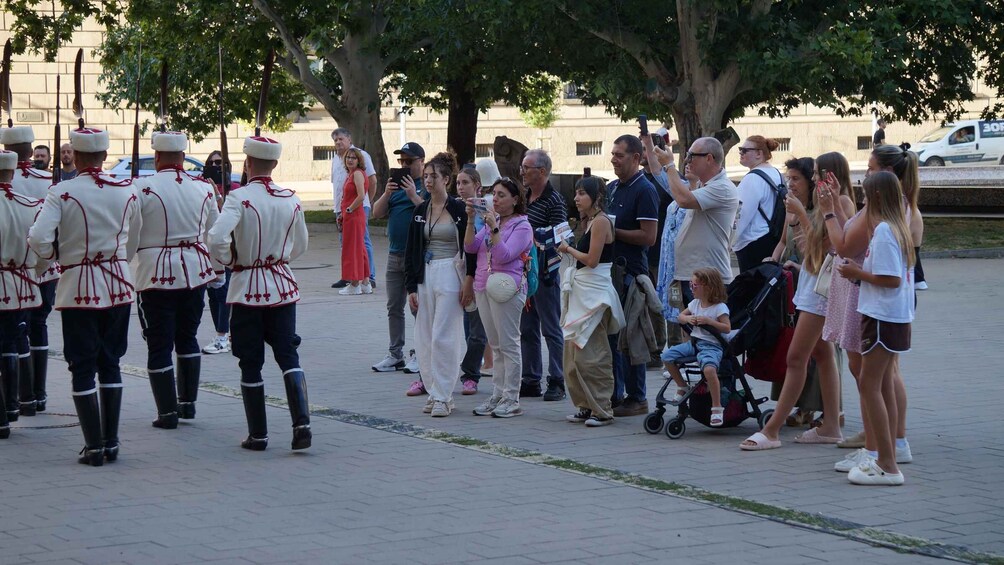 A group of uniformed personnel standing in formation, with civilians observing and taking photos. 3