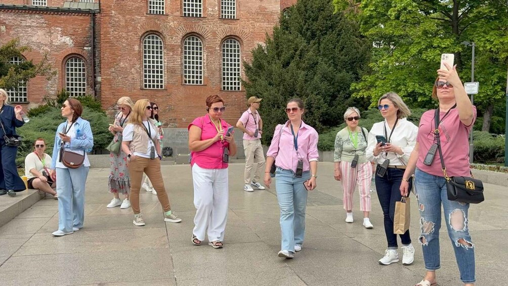 Een groep mensen loopt voorbij een historisch gebouw van baksteen met boogvensters. 5