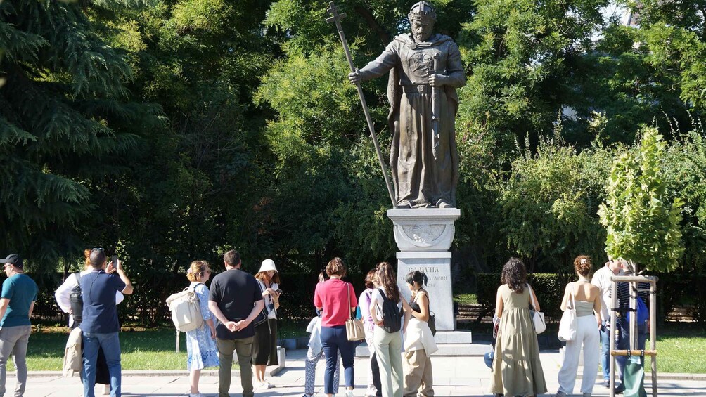 A statue of a historical figure in a park with people gathered around it. 4