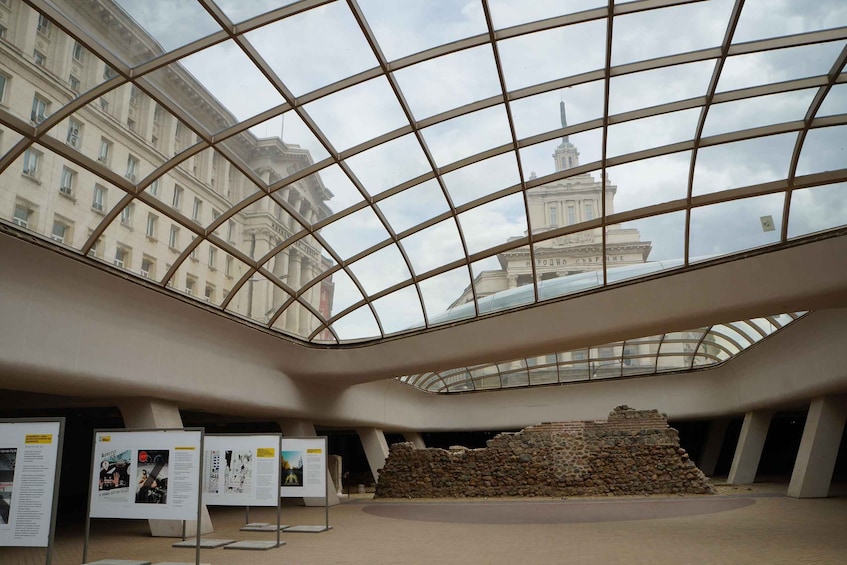 A museum interior with a glass ceiling, stone ruins, and informational displays. 3
