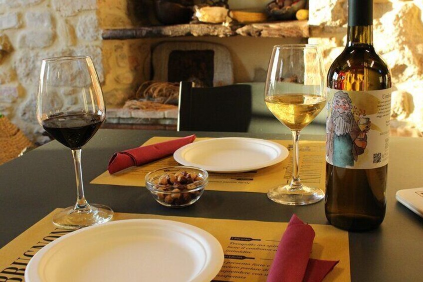 A table set with a bottle of wine, two glasses, a bowl of nuts, and a menu. 3