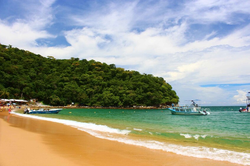A beach with clear turquoise water, a sandy shore, and boats anchored near the shore. 3