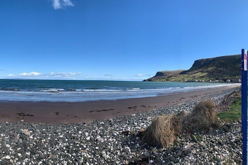Una playa rocosa con un cielo azul despejado y una colina distante. 4
