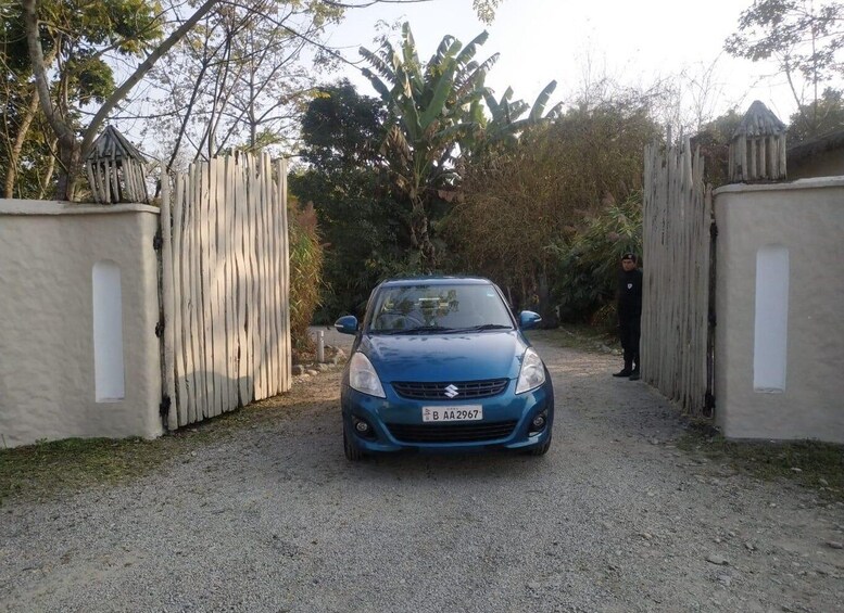 A blue car parked at a gated entrance surrounded by trees and vegetation. 5