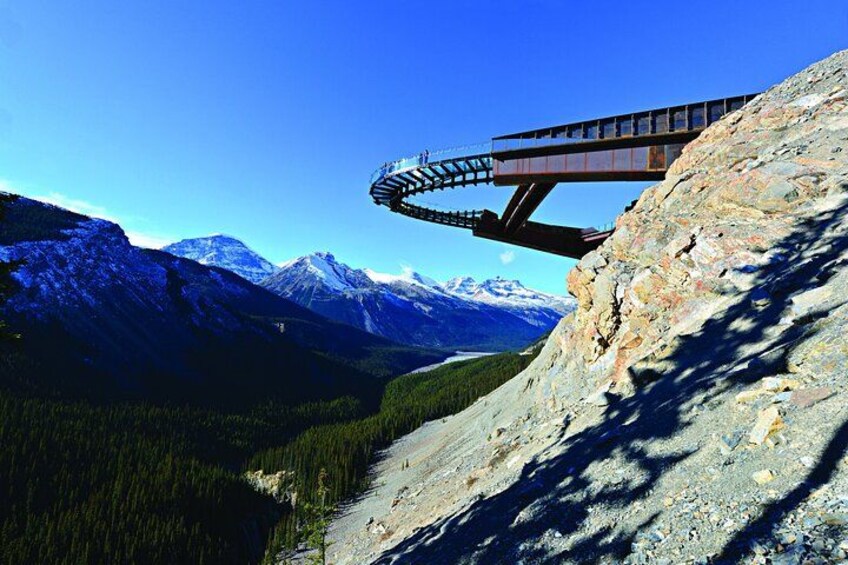 A mountain landscape with a suspension bridge, snow-capped peaks, and a forested valley. 1