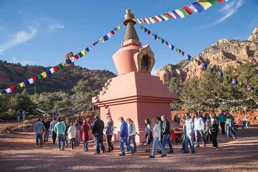 A group of people gathered around a pink stupa with prayer flags, set against a mountainous backdrop. 4