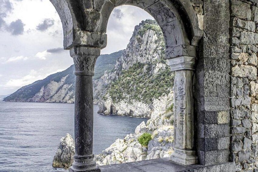 A stone archway overlooking a coastal landscape with rocky cliffs and a body of water. 1