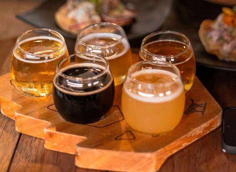 Un plateau en bois avec six verres de bière, dont l’un est de couleur foncée. 1