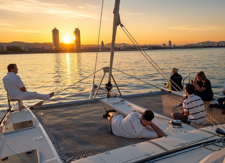 Un grupo de personas navegando en un velero al atardecer, con un horizonte urbano de fondo. 1