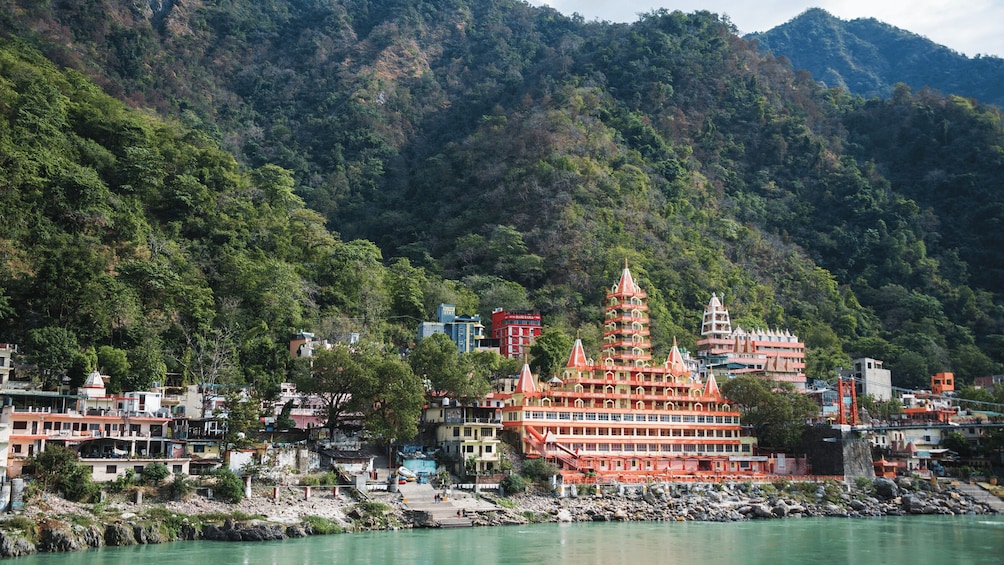 A riverside town with a prominent multi-tiered temple, lush green hills, and a mix of residential and commercial buildings. 5