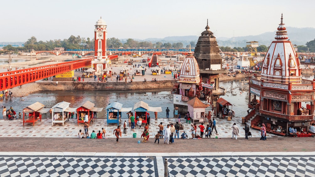 A riverside temple complex with a red bridge, a clock tower, and a large stupa. 2