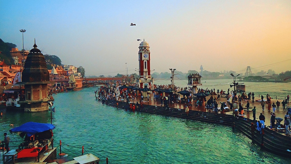 A crowded riverside with a prominent clock tower and a bridge in the background. 3
