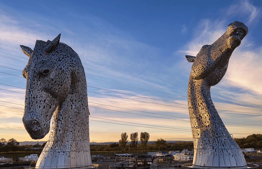 Two large metallic sculptures resembling horses, set against a clear sky with power lines in the background. 3
