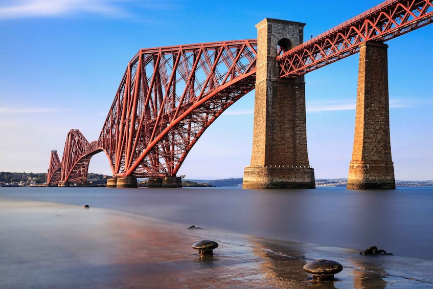 A red steel bridge with two large towers over calm water. 2