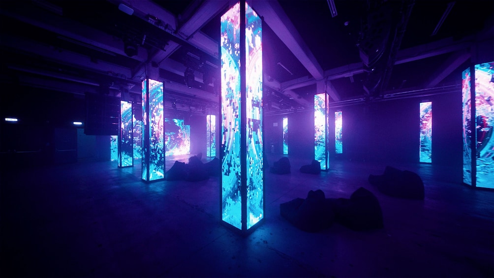 A dark room with illuminated vertical panels displaying abstract digital art. 3