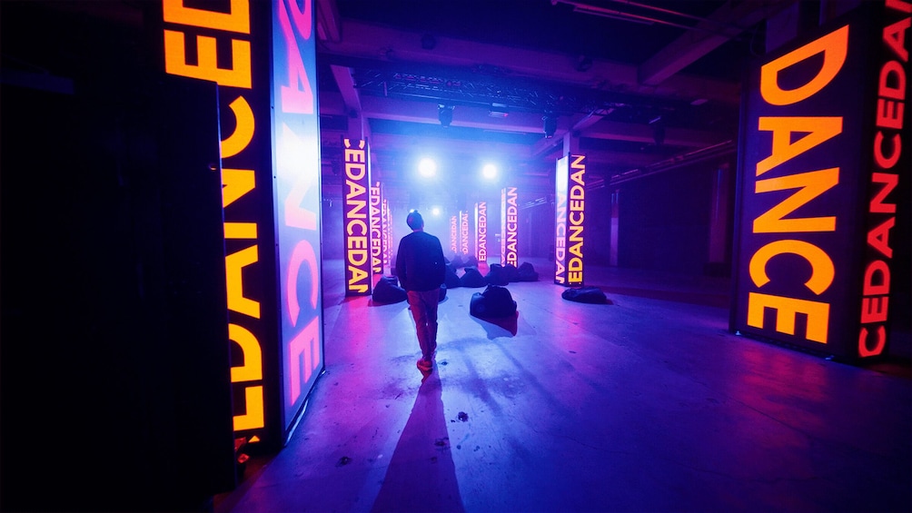 A person walking through a corridor with illuminated signs reading 'CEDANCE DANCE'. 2