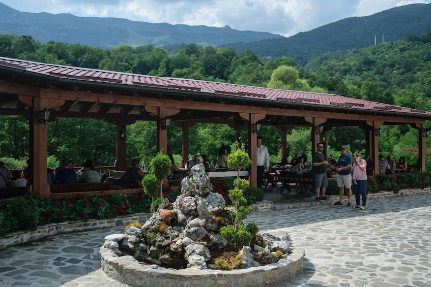A covered outdoor seating area with a stone fountain, surrounded by lush greenery and mountains in the background. 5