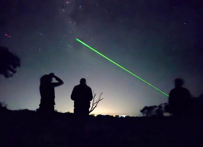 Silhouettes of people against a night sky with a green laser beam. 5