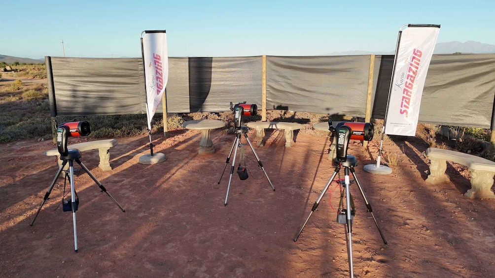 A desert landscape with three tripods set up under a tent, each with a device on top, and banners hanging from the tent. 4