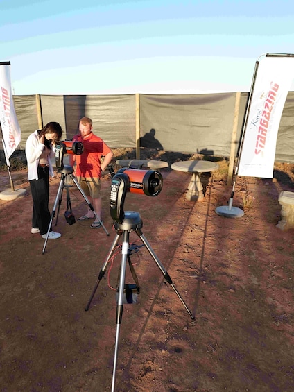 A person operating a telescope on a tripod outdoors. 2