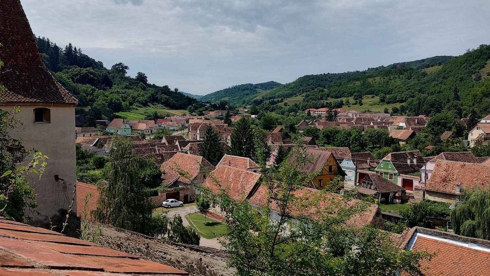 Un pueblo con techos de tejas rojas ubicado en un valle rodeado de colinas verdes. 2