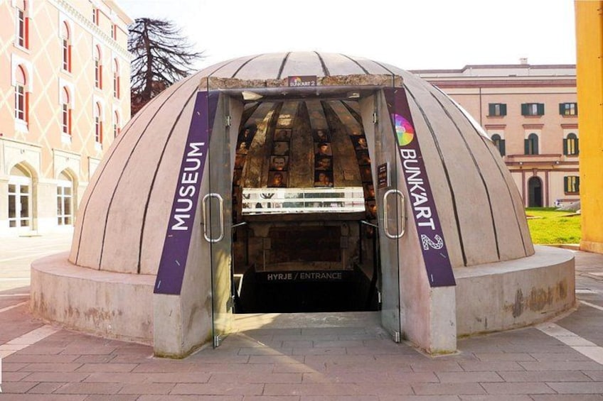 Entrada a un museo con una estructura en forma de cúpula, un cartel que dice 'MUSEUM' y un banderín que reza 'BUNKART'. 1