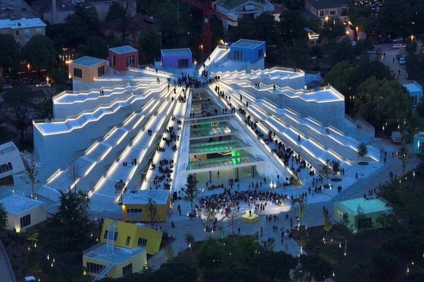 Una amplia plaza pública con un espacio central abierto rodeada de edificios con escalones iluminados. 4