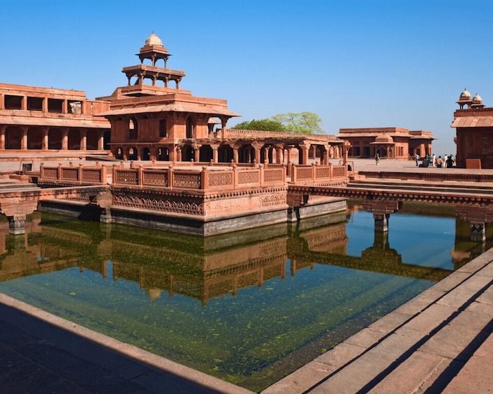 A historic water tank with intricate architecture, surrounded by a reflective pool and a clear blue sky. 2