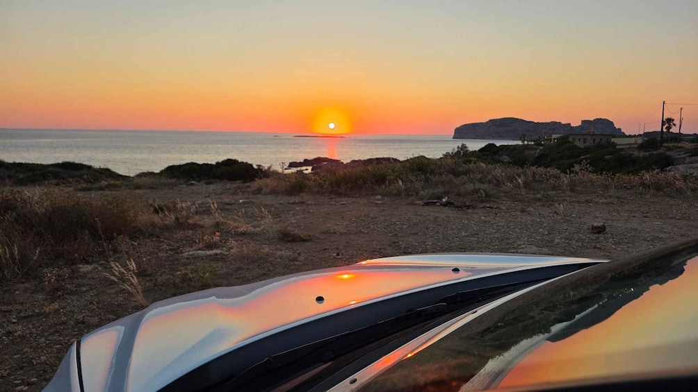 A sunset over a beach with a car in the foreground. 1