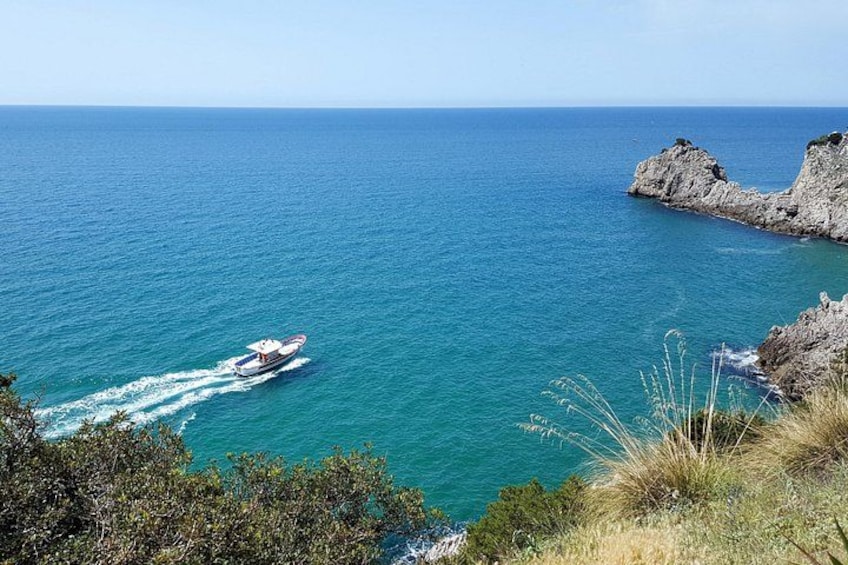 A boat on a turquoise sea, rocky coastline, and grassy hilltops. 2